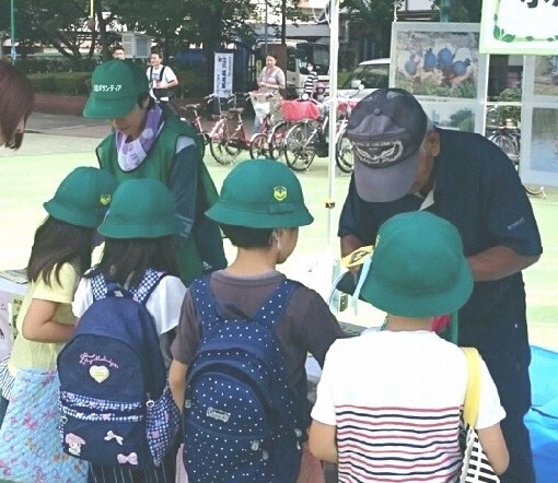 写真:緑色の帽子をかぶった児童らとブースの大人たち