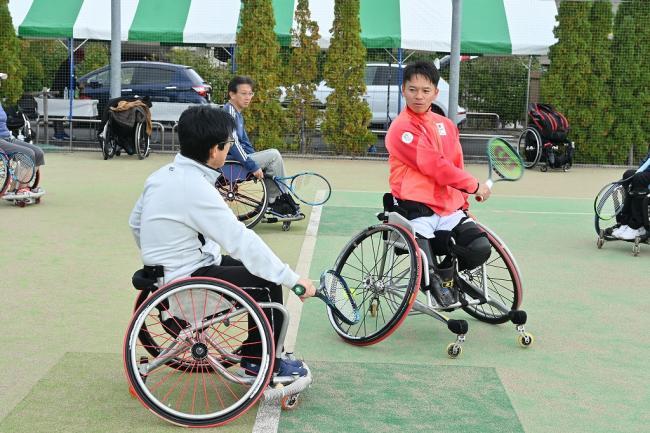 写真:競技用車いすに乗りながらラケットの振り方を教わる参加者