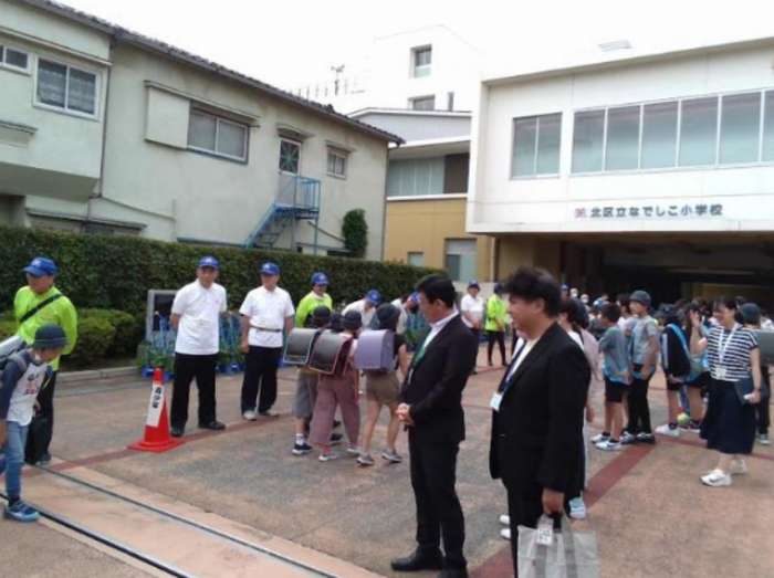 校門で児童が先生や代表児童とあいさつしている様子